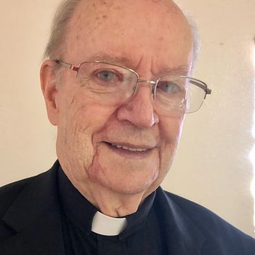 Elderly man wearing glasses and a clerical collar smiling.