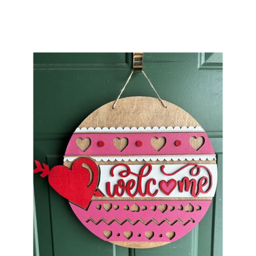 Decorative round wooden door hanger with 'welcome' and heart cutouts.