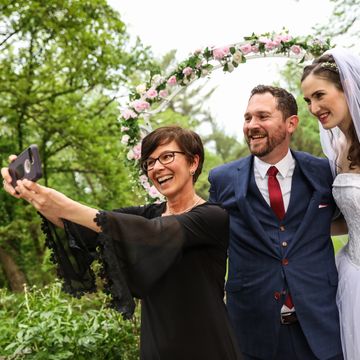 Bride, groom and Justice of the Peace taking a selfie with a floral arch and trees behind them.