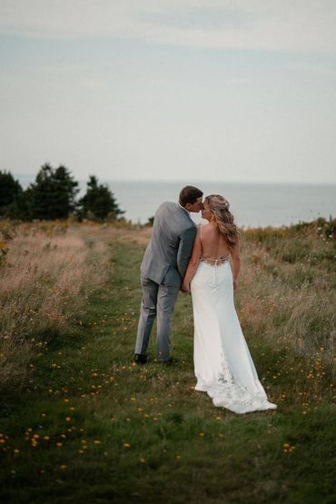 Bride and groom walking through the meadow towards the clifftop overlooking the ocean.