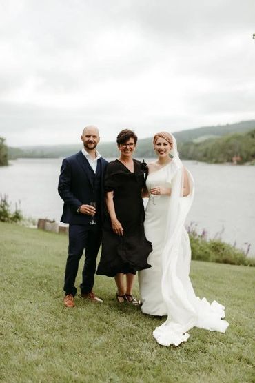 A bride, groom and Justice of the Peace standing together in front of a lake in Nova Scotia.