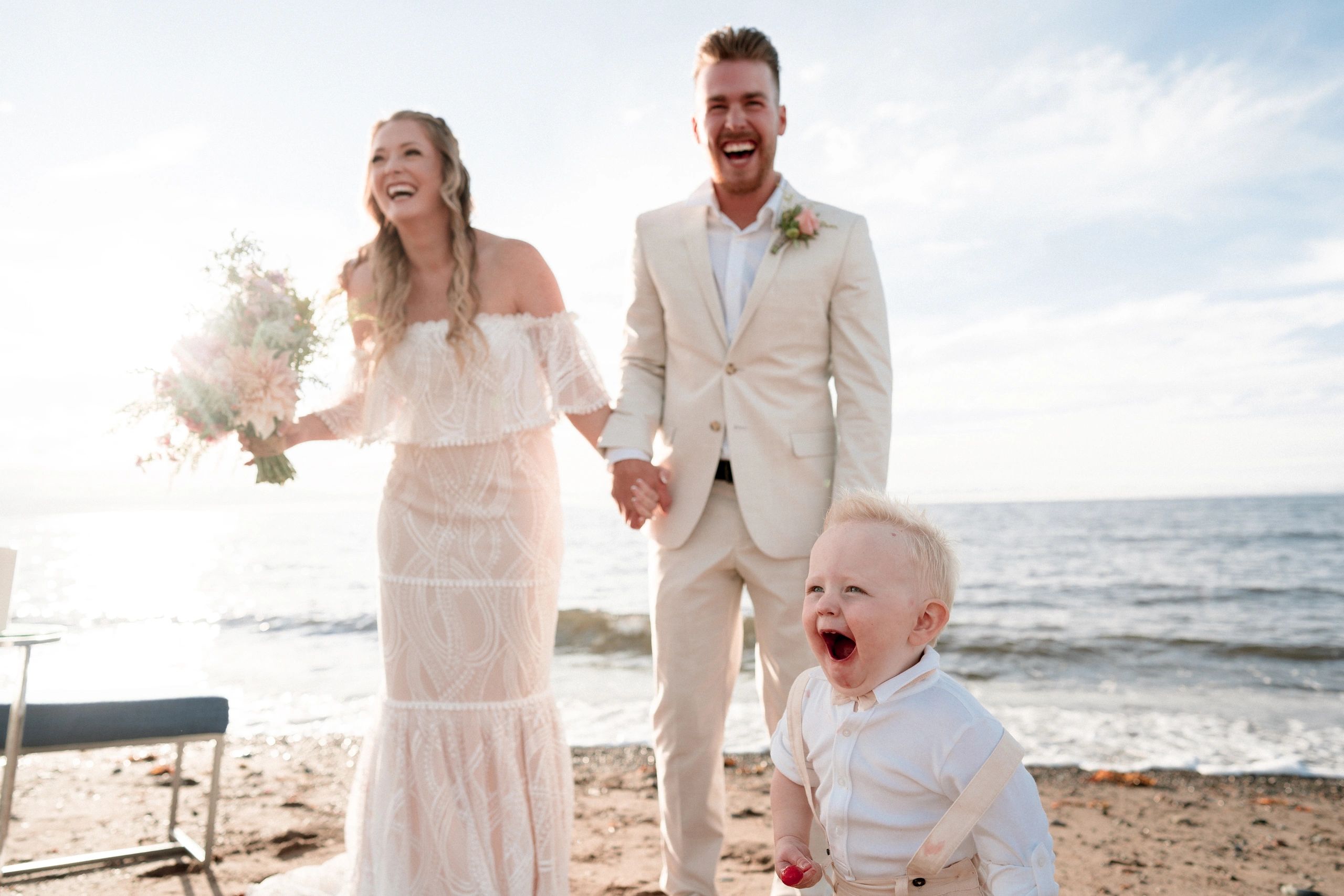 bride and groom laughing along with toddler on a beach elopement