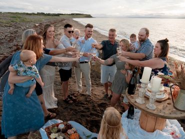 A family raising glasses of champagne to toast a newly married couple on a beach at sunset.