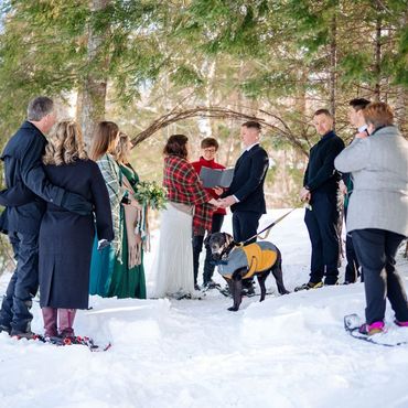 An elopement in the snowy forest, everyone is wearing snowshoes while watching the ceremony.