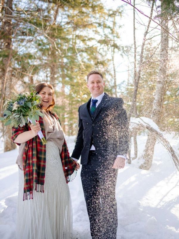 An elopement couple standing in show shoes in a forest with snow sparkling around them.