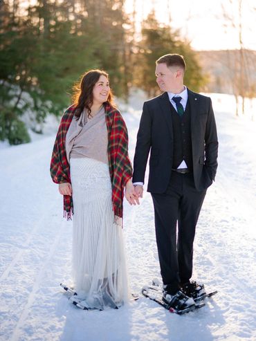 Bride and groom looking at each other while standing on the snow in a forest wearing snowshoes.