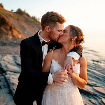 Bride and groom kissing on a rocky beach with the sun setting behind them. 