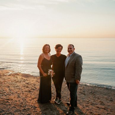 Bride, groom, Justice of Peace standing on 
beach at sunset celebrating elopement in Nova Scotia.