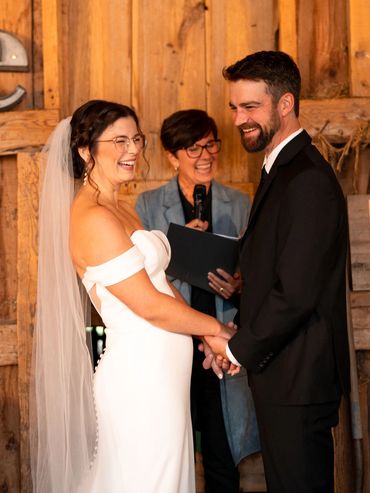 A bride, groom and Justice of the Peace laughing while getting married in a wooden barn.