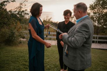 A bride, groom and Justice of the Peace smiling as they perform a handfasting ceremony at sunset.