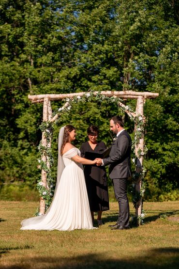 Justice of the Peace officiating a wedding under a birch bark arbor by the forest in Nova Scotia.