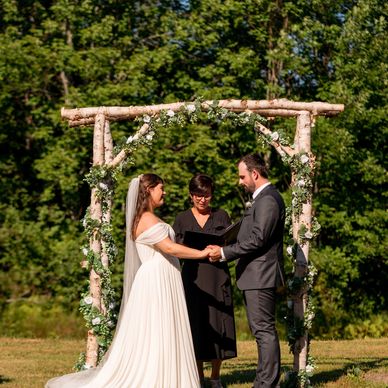 Bride and groom getting married by Justice of the Peace standing under birch bark arbor.