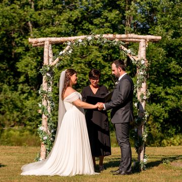 Justice of the Peace officiating a wedding under a birch bark arbour by the forest in Nova Scotia.