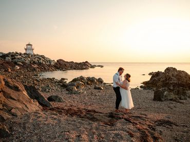 Nova Scotia elopement with a couple on a beach with a lighthouse and sunset in the distance. 