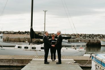 Nova Scotia elopement showing two grooms getting married in front of a sailboat in a lobster wharf. 