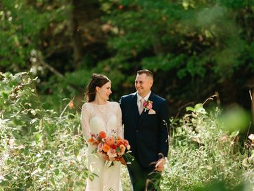 Bride and groom smiling after their Ontario elopement, standing in a field of tall green grass. 