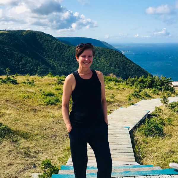 Woman standing on wooden hiking trail on Cape Breton overlooking the ocean.