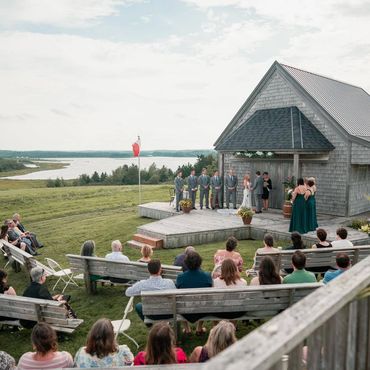 A Justice of the Peace officiates a wedding in front of a wooden building overlooking the ocean.