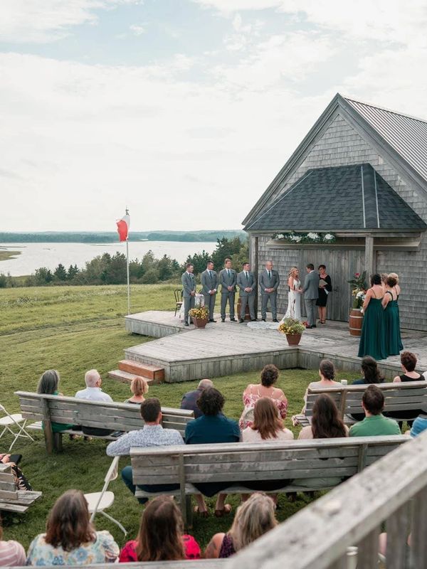A Justice of the Peace officiates a wedding in front of a wooden building at Pomquet Beach.