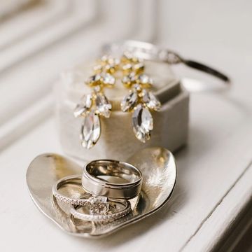 Silver dish in the shape of a heart holding wedding rings and diamond earrings.