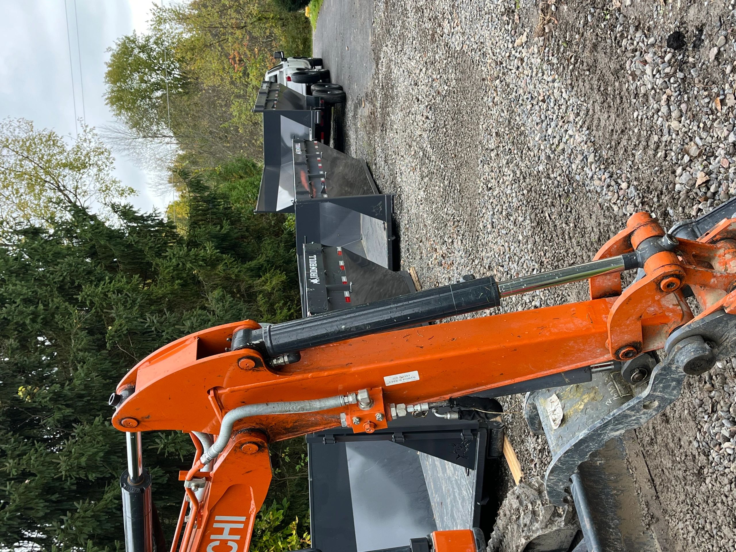 Close-up of an orange excavator arm with trailers and a truck in the background.
