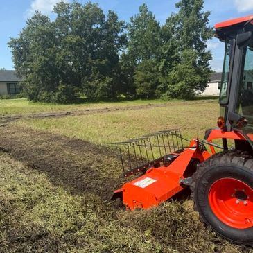 Orange tractor tilling soil in a green field.