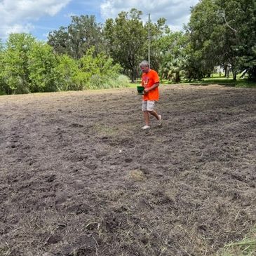 Man in orange shirt walking on freshly tilled soil.