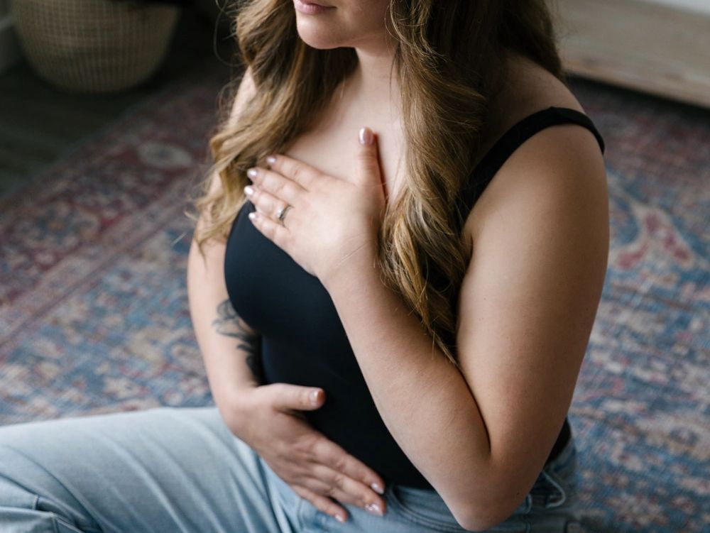 A woman practices mindfulness, sitting cross-legged with hands on chest and abdomen.