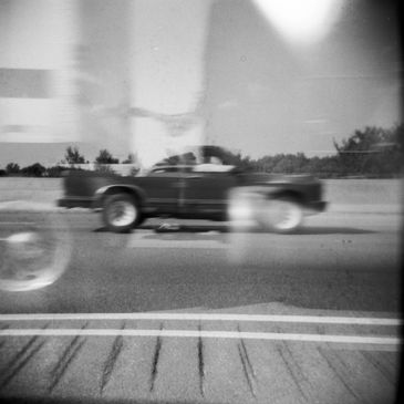 Black and white photo of a blurred pickup truck driving on a road.