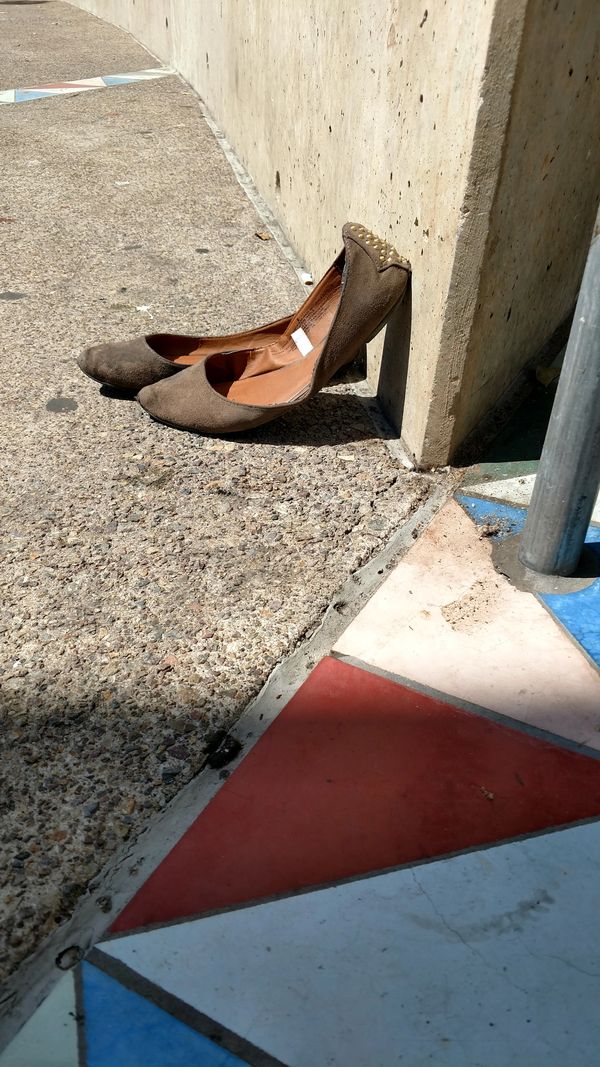 Pair of brown flats leaning against a concrete wall on a textured sidewalk.