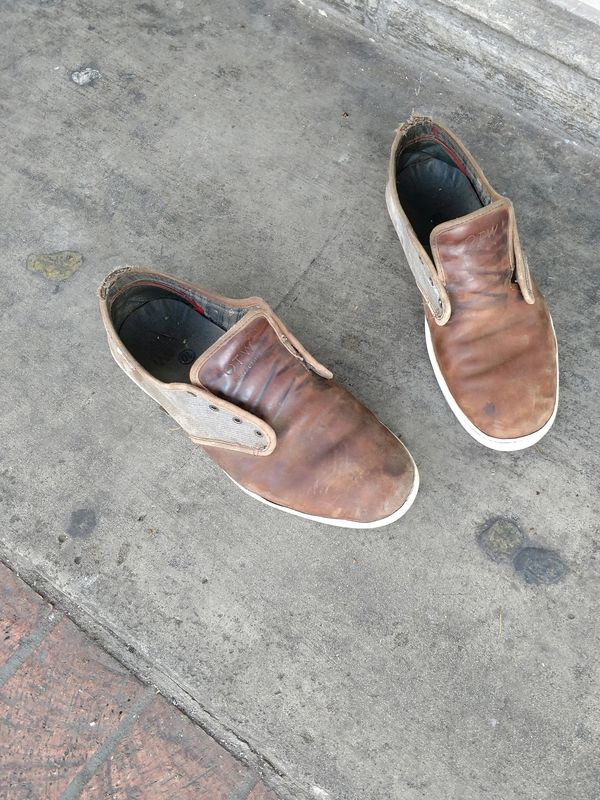 Worn leather slip-on shoes on a concrete surface.