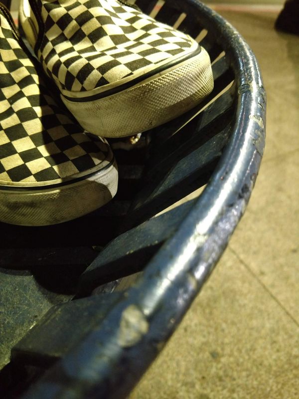 Worn checkered slip-on shoes resting on a blue metal bench.