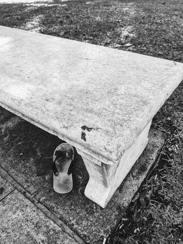 Stone bench with a single sandal on the ground beside it.