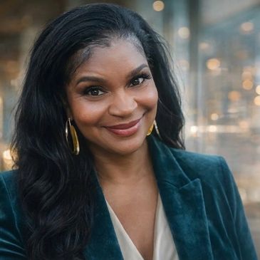 Woman with long dark hair smiling, wearing gold hoop earrings and a teal blazer.