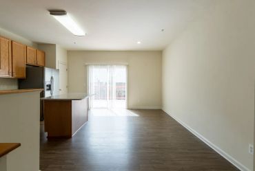 Empty modern kitchen and living area with wood flooring.