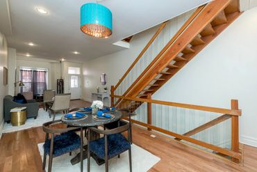 Modern dining and living area with wooden staircase and blue accents.