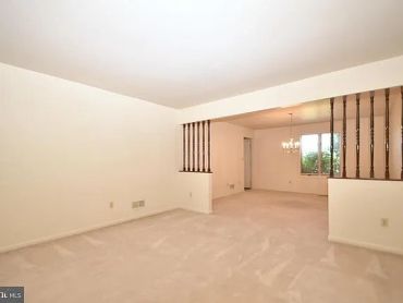 Empty beige living room with carpet and chandelier.