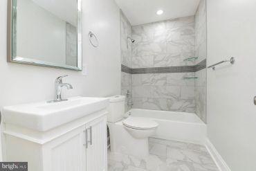 Modern white bathroom with bathtub and marble tiles.