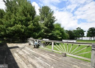 Spacious wooden deck with rustic railing and green surroundings.