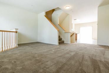 Empty living room with carpeted floor and staircase.