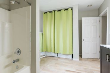 Modern bathroom with green shower curtain and light wood flooring.