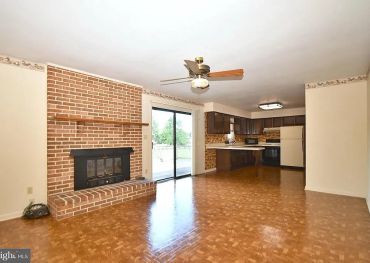 Empty living room with brick fireplace and kitchen.