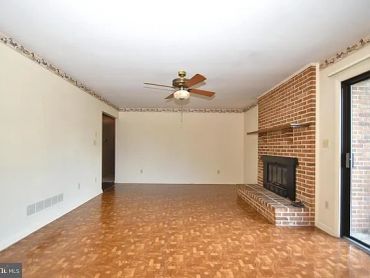 Empty living room with brick fireplace and ceiling fan.
