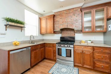Modern kitchen with wooden cabinets, stainless steel appliances, and a brick accent wall.