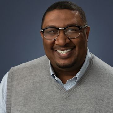 Smiling man wearing glasses and a grey sweater vest.