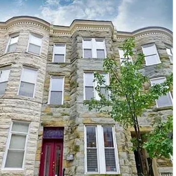 Stone facade townhouse with a red door and tree in front.