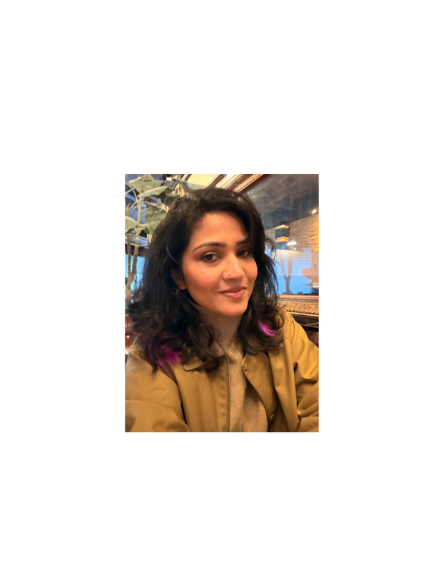 A woman with wavy black hair and purple highlights smiles softly indoors.