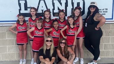 A youth cheerleading team in red uniforms posing with their coaches.