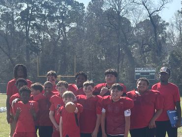 Youth football team posing together on a field during daytime.