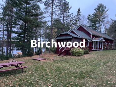 A red cabin named Birchwood surrounded by trees.